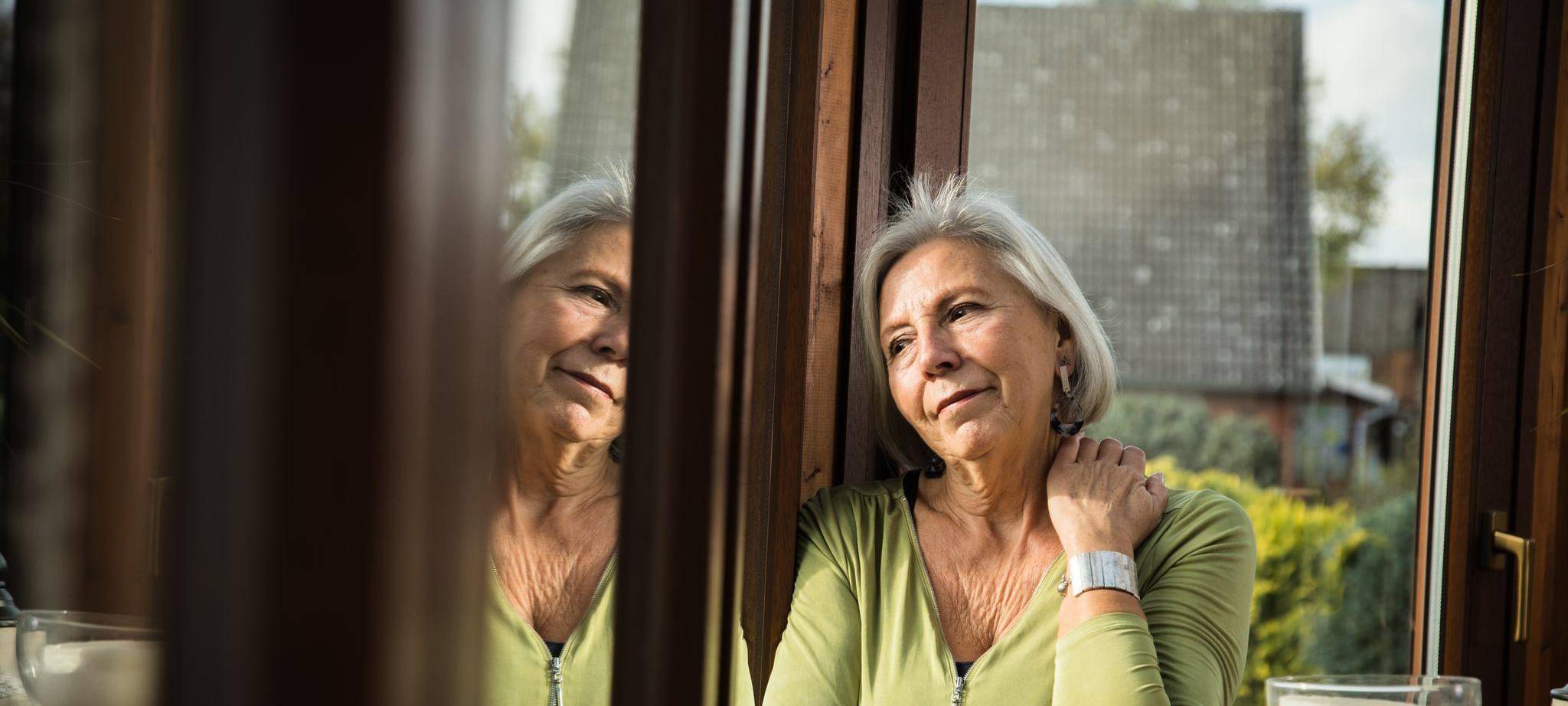 Eine ältere Frau schaut gedankenverloren aus dem Fenster