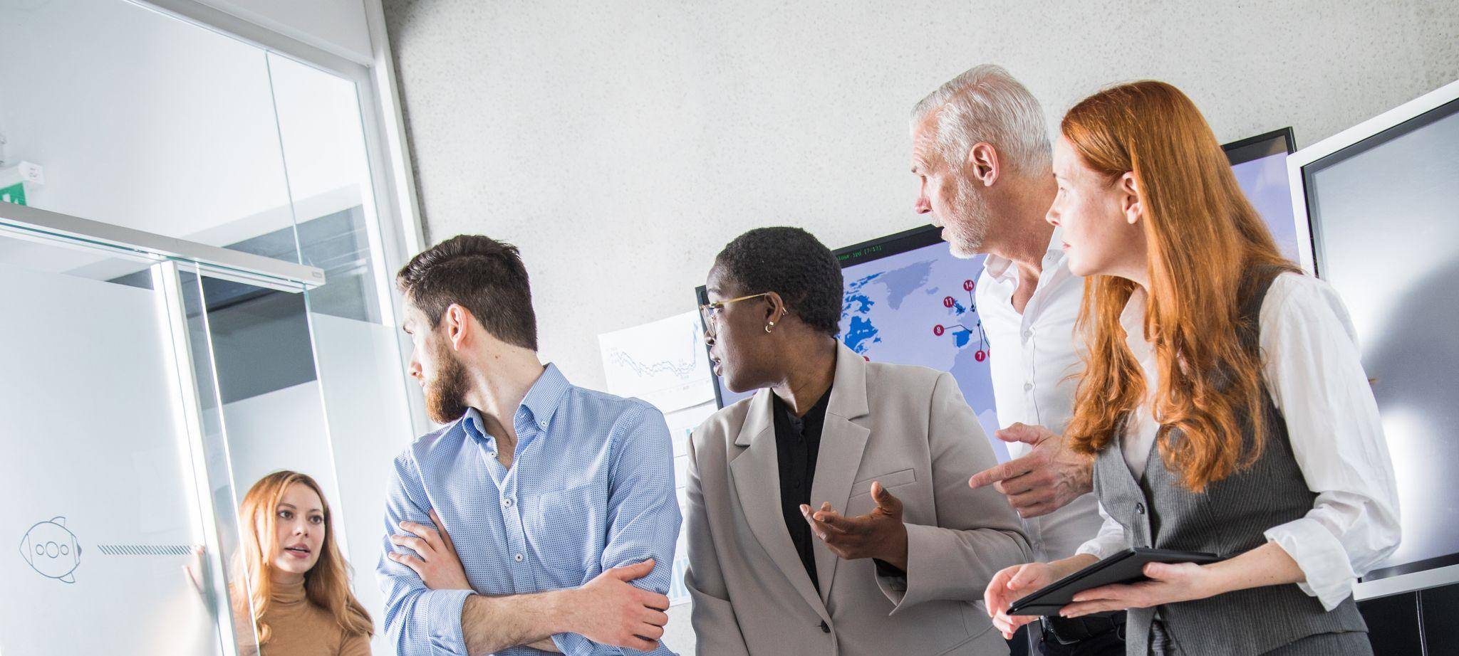 Eine Kollegin hebt die Uhr in einem Meeting mit anderen Kollegen