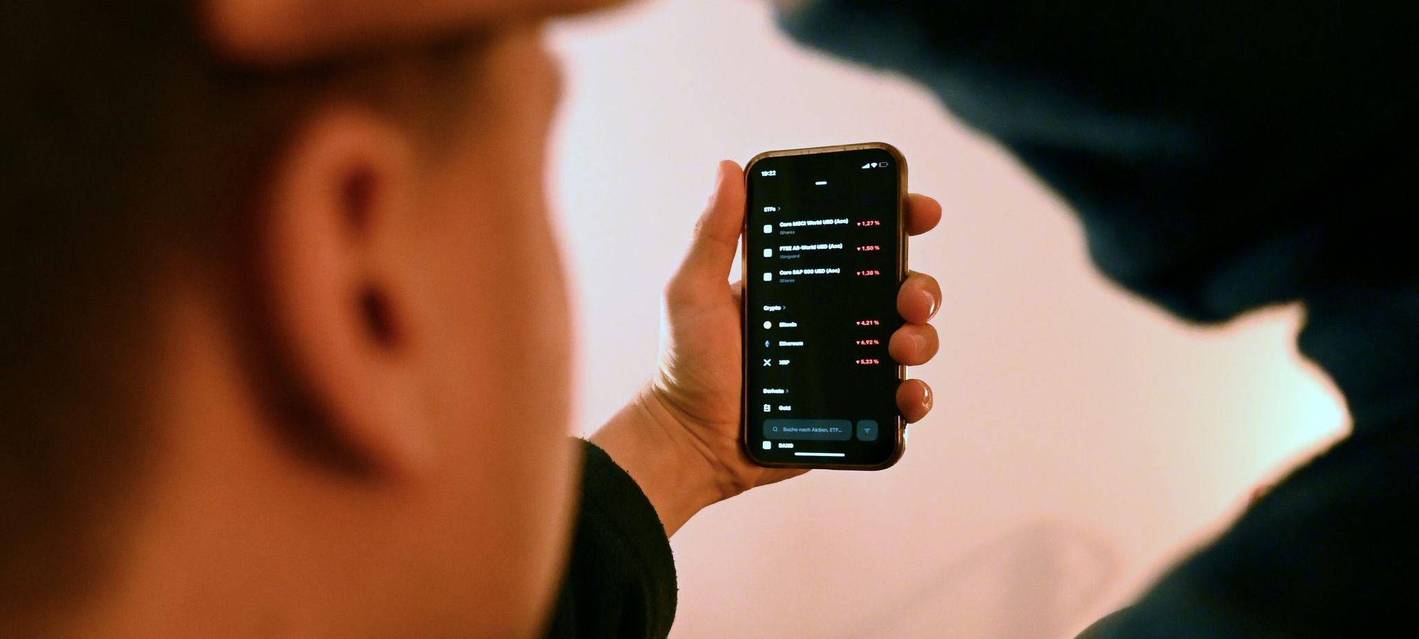 Mann schaut sich Trading-App eines Neobrokers mit Aktienkursen an
