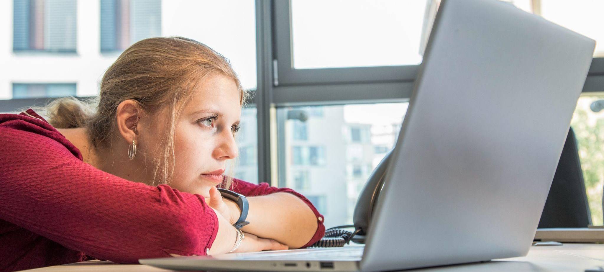 Frau schaut lustlos auf den Bildschirm eines Laptops
