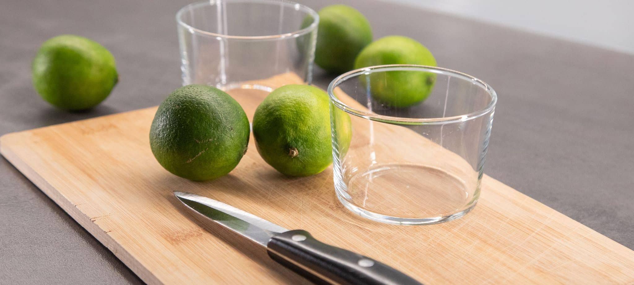Limetten liegen neben zwei Schälchen auf einem Brett