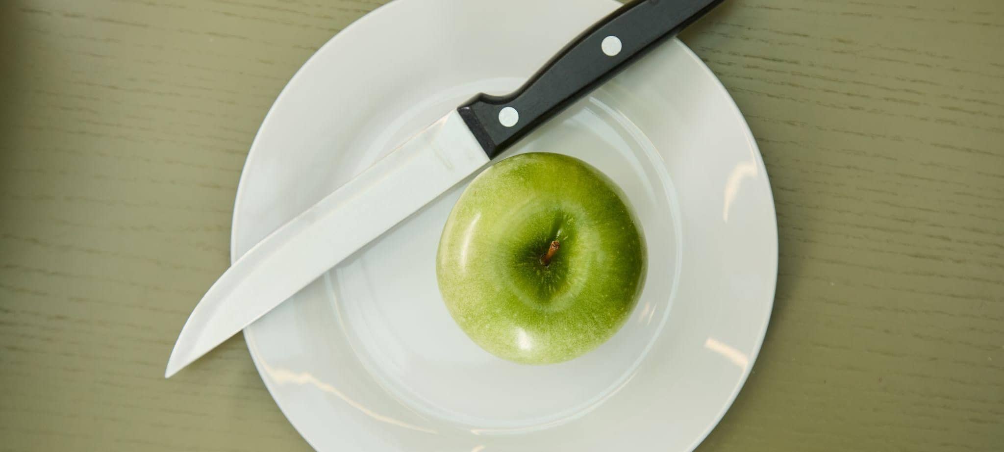 Ein Apfel liegt neben einem Messer auf einem Teller